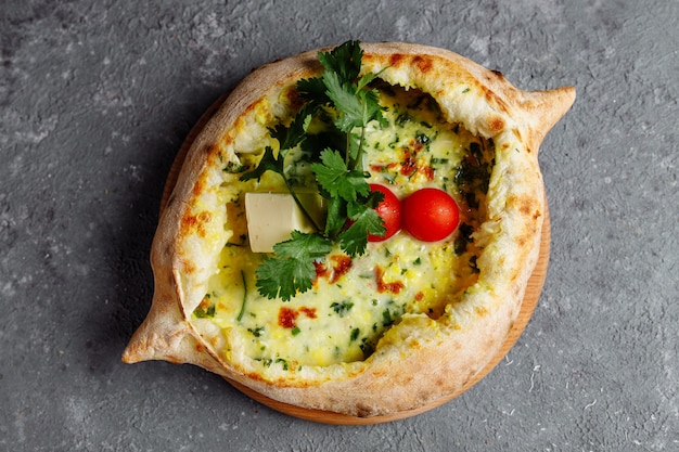 Adjarian Khachapuri mit Käse, Spinat, Tomaten und Kräutern. Auf einer grau-blauen Tafel georgische Küche. Flach liegen. Draufsicht