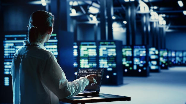 Administrador de sistemas asiático ejecutando código y programación en computadoras portátiles solucionando problemas y actualizando equipos de granja de servidores diseñados para acomodar computadoras centrales, racks de red y matrices de almacenamiento