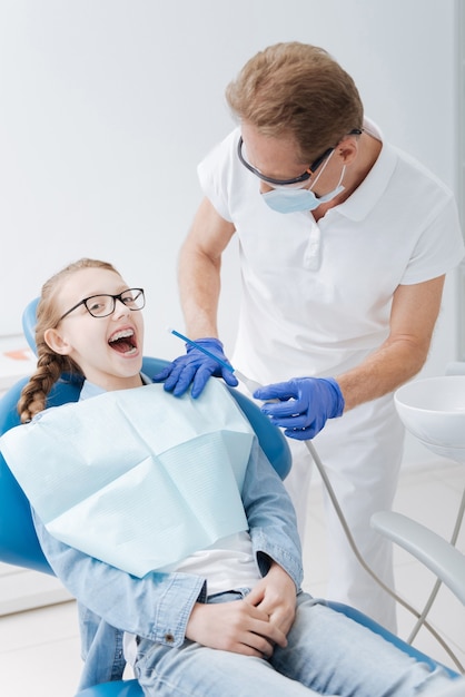 Admirável senhora sorridente e brilhante sentada na cadeira do dentista e esperando o procedimento necessário enquanto o médico prepara seu equipamento