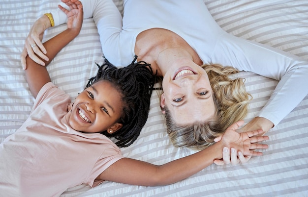 Adoção de mãe e criança deitada na cama com um sorriso para um tempo de união familiar de qualidade juntos em casa Mãe feliz segurando criança adotada sorrindo e relaxando de felicidade por diversão lúdica no quarto acima