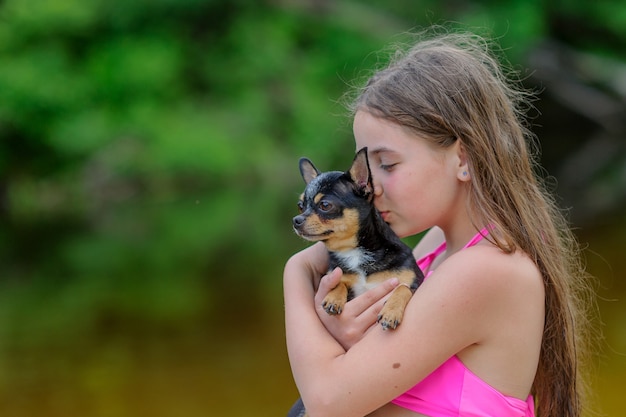 Adolescente à beira do rio em maiô rosa com um cachorro chihuahua nos braços