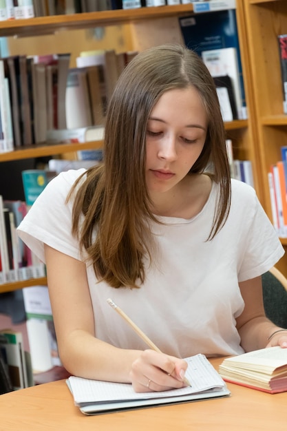 Adolescente a escrever num livro na biblioteca.