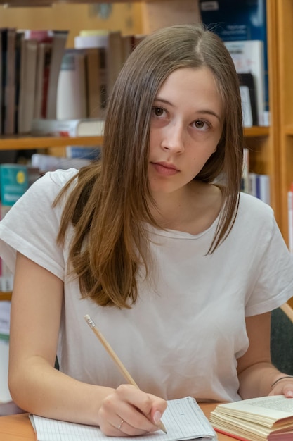 Adolescente a escrever num livro na biblioteca.