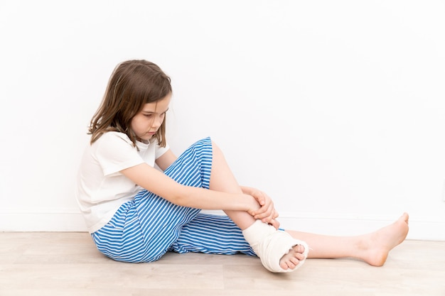 Adolescente aburrida con yeso en el pie sentada en el suelo. cirugía para corregir la deformidad del pie en niños. Pacientes con movilidad reducida.