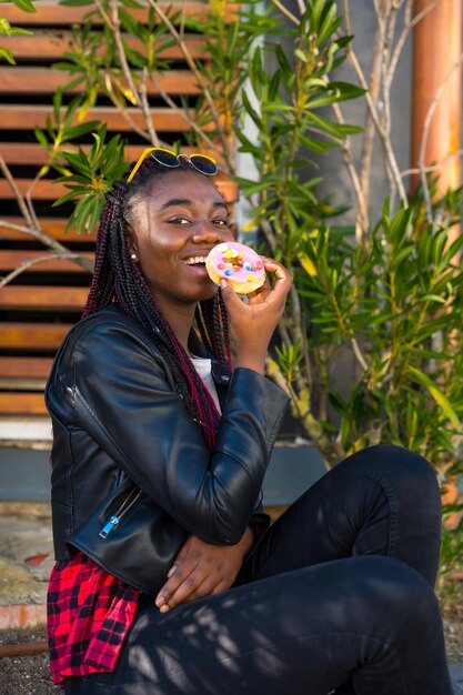 Adolescente africano comiendo una rosquilla sentado solo en la calle