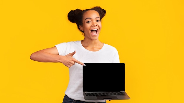 Adolescente africano feliz apuntando a la pantalla en blanco de su computadora portátil