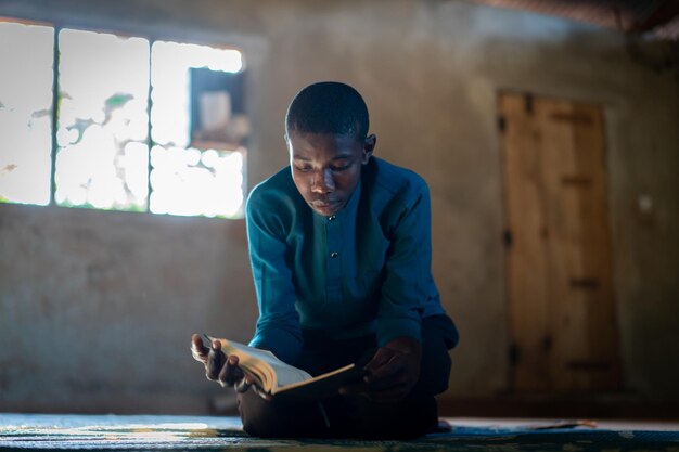 Adolescente africano sentado e lendo livro em escola pobre, foto de alta qualidade