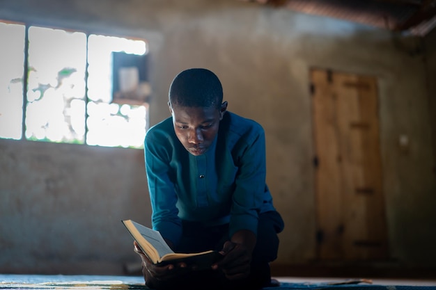 Adolescente africano sentado e lendo livro em escola pobre, foto de alta qualidade