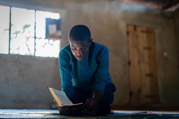 Adolescente africano sentado e lendo livro em escola pobre, foto de alta qualidade