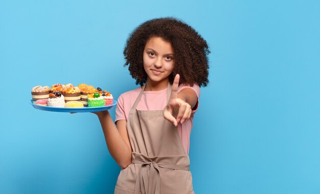 Adolescente afro bonito sorrindo com orgulho e confiança fazendo a pose número um triunfantemente