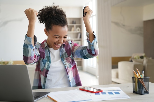 Una adolescente afroamericana emocionada recibió un correo electrónico con buenas noticias en una laptop grita y hace un gesto de sí