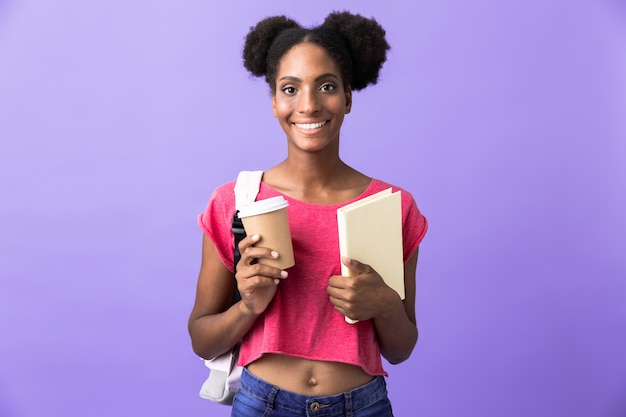 Adolescente afroamericana estudiante sosteniendo libro de ejercicios y café para llevar, aislado