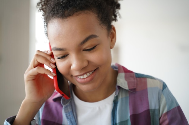 Adolescente afroamericana hablando por teléfono celular con un amigo Adolescente está chismeando y coqueteando