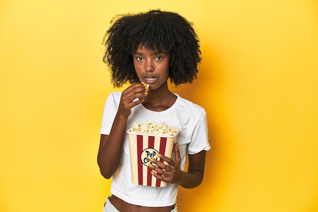 Adolescente afroamericana con palomitas de maíz disfrutando de conceptos de cine sobre un fondo amarillo