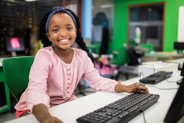Adolescente afroamericana sentada en un escritorio blanco en un laboratorio moderno alcanzando el teclado negro