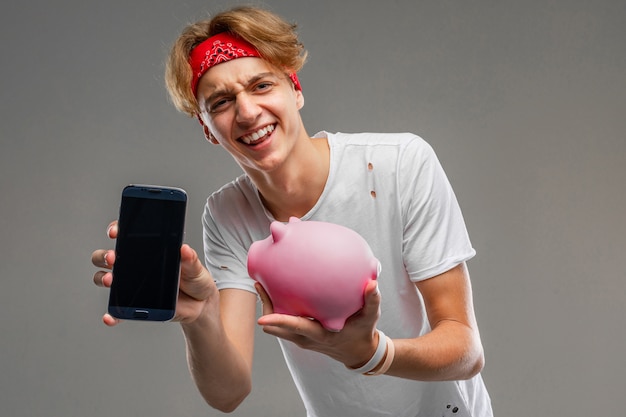 Adolescente con alcancía posando contra gris, joven con una camiseta ligera contra un fondo de pared gris