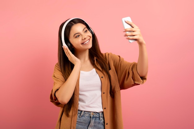 Una adolescente alegre con auriculares inalámbricos tomando selfies con su teléfono inteligente