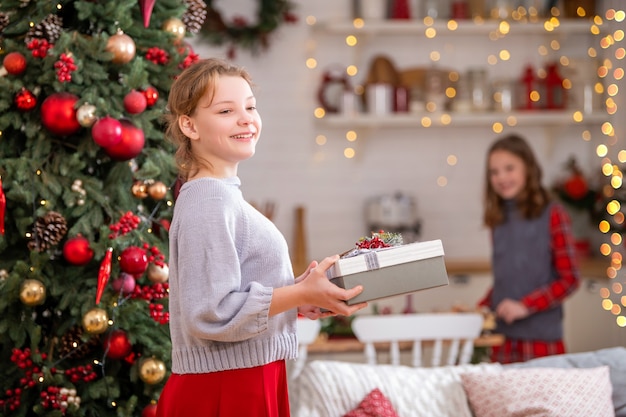 Adolescente alegre con una caja con un regalo en sus manos en casa en el fondo del árbol de Navidad