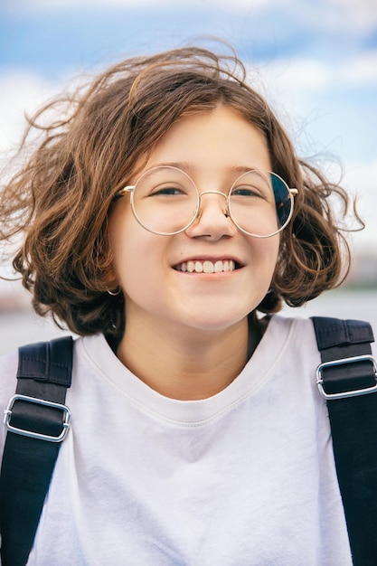 Adolescente alegre em óculos da moda legal com cabelo encaracolado ao ar livre