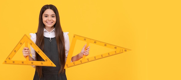 Una adolescente alegre sostiene una regla de triángulo matemático en la escuela sobre educación de fondo amarillo Banner de una estudiante de la escuela Retrato de una alumna de la colegiala con espacio de copia