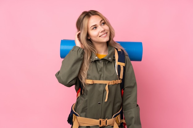 Adolescente alpinista con una mochila grande en la pared rosa pensando en una idea