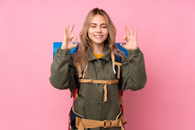 Adolescente alpinista con una mochila grande en rosa en pose zen