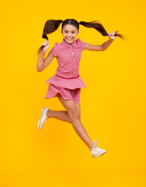 Adolescente animado, adolescente engraçado, salto de criança, aproveite a alegria da vitória isolada em fundo amarelo Menina pequena em vestido pulando
