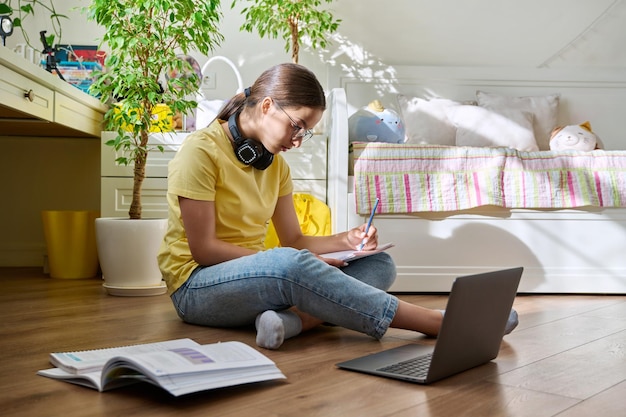 Adolescente con anteojos estudiando en casa usando una laptop