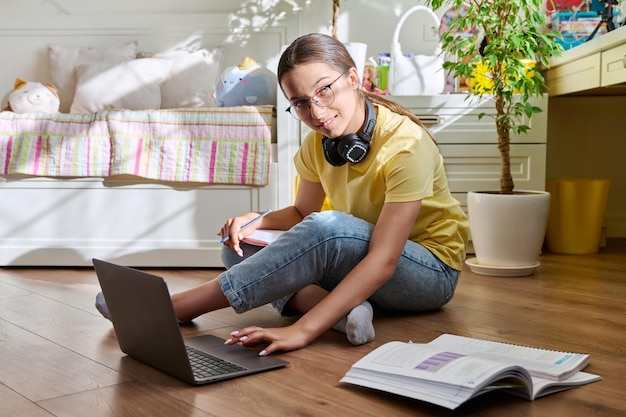 Adolescente con anteojos estudiando en casa usando una laptop