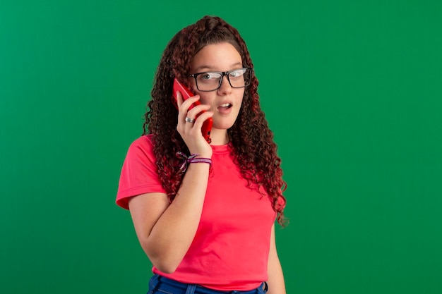 Adolescente con anteojos usando teléfono celular en poses divertidas en foto de estudio con fondo verde ideal para recortar