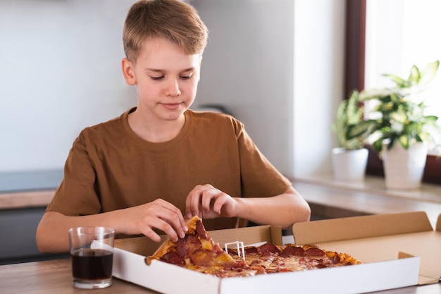 Un adolescente arranca un trozo de pizza en la cocina de su casa Entrega de alimentos