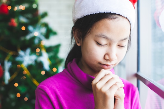 Adolescente asiática cerró los ojos y cruzó la mano en oración para desear en la celebración de navidad