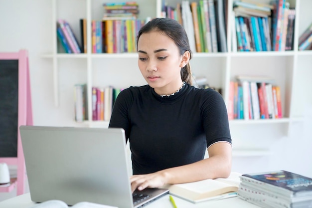 Una adolescente asiática estudiando con una computadora portátil en la biblioteca