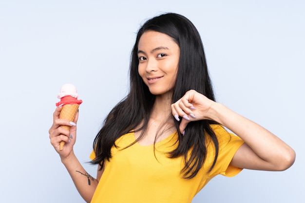 Adolescente asiática con un helado de cucurucho en la pared azul orgulloso y satisfecho de sí mismo