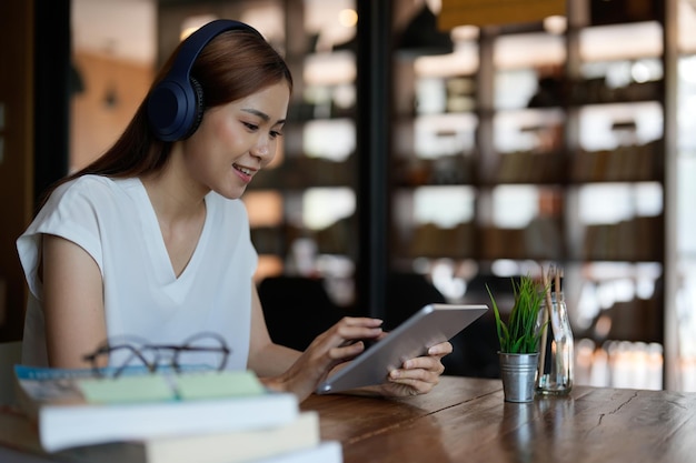 Adolescente asiática sonriente con auriculares mirando la tableta, escuchando y aprendiendo cursos en línea Mujer de negocios china feliz con auriculares, videollamada, concepto de educación en línea