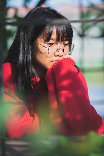 Adolescente asiática vistiendo un suéter rojo sentado al aire libre