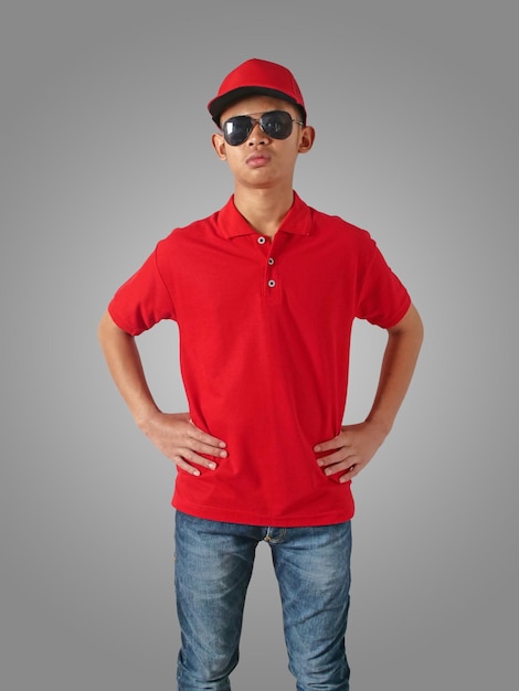 Foto un adolescente asiático con una camiseta de polo roja de pie con las manos en la cadera.