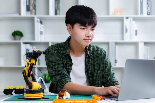 Adolescente asiático construyendo proyecto de tarea de brazo robot con computadora portátil en casa