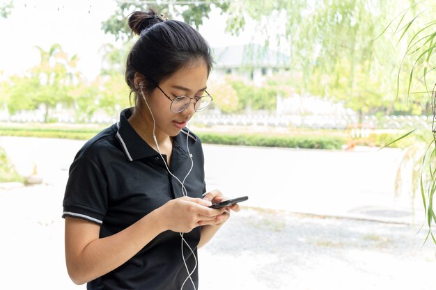 Adolescente asiático con vidrios que escucha música en el teléfono celular.