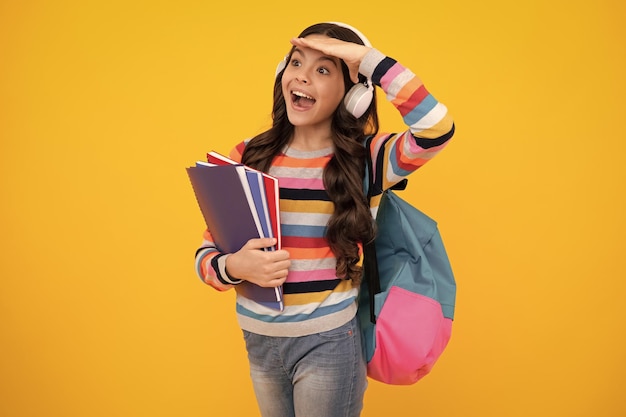 Adolescente asombrado Escolar adolescente estudiante niña con auriculares y mochila escolar en amarillo