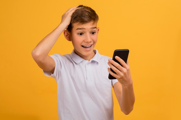 Foto un adolescente asombrado mirando la pantalla de su teléfono inteligente y tocando la cabeza