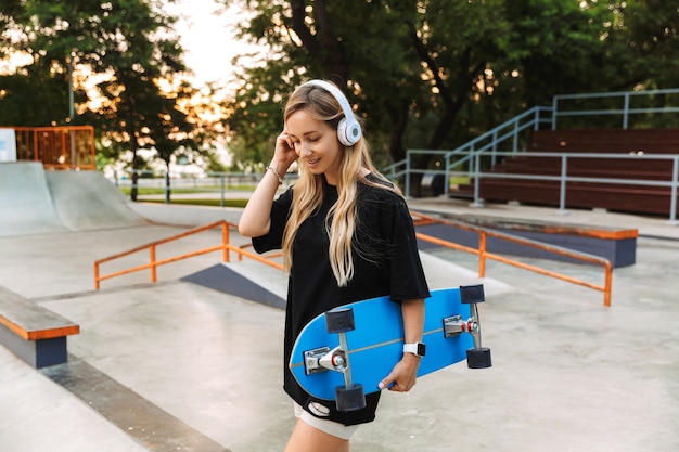 Adolescente atraente e descolada carregando longboard enquanto caminha no skatepark