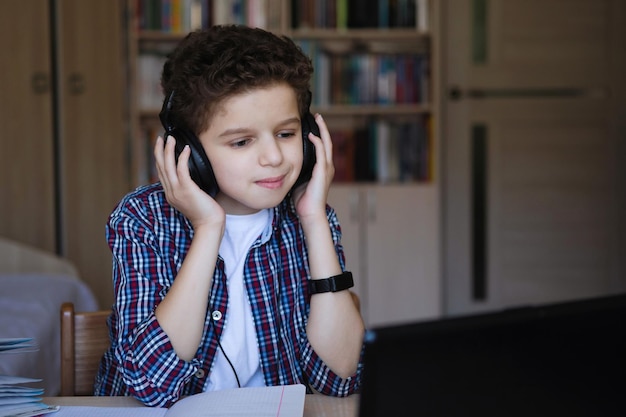 Adolescente con auriculares cuidadosamente escucha música sentado en la mesa Entrenamiento en casa sobre cuarentena de coronavirus Enfoque selectivo Fondo borroso