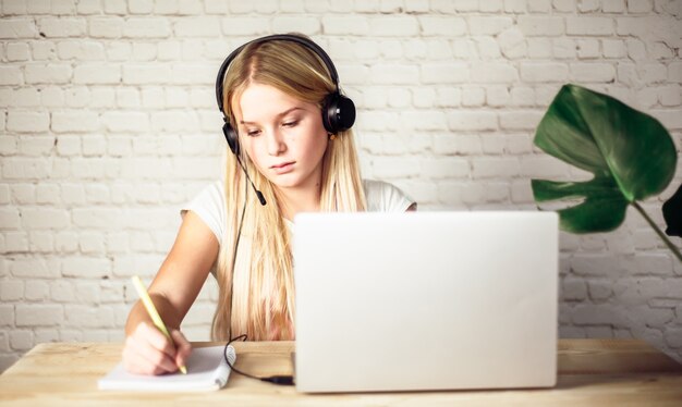 Adolescente en auriculares estudiando en línea y usando su computadora portátil en casa