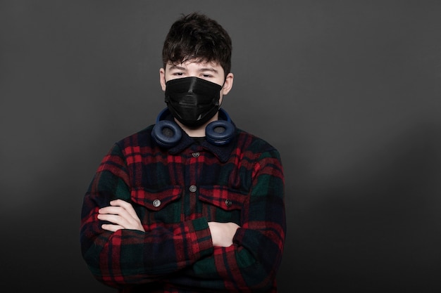 Adolescente con auriculares y máscara médica en estudio con fondo gris