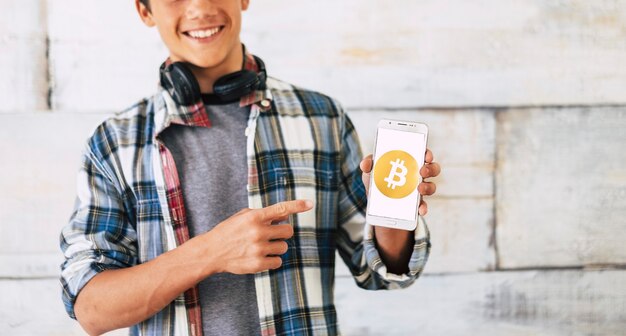 Adolescente con auriculares de pie y mostrar bitcoin en su teléfono: sonríe.