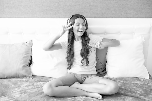 Adolescente con auriculares se relaja en la cama en casa usando auriculares cantando adolescente feliz emociones positivas y sonrientes