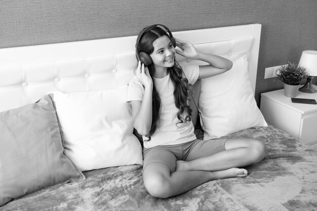 Una adolescente con auriculares se relaja en la cama en casa usando auriculares cantando