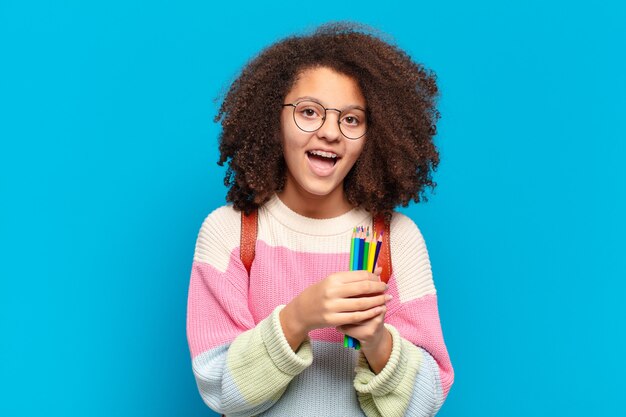 Adolescente bastante afro parecendo feliz e agradavelmente surpreso, animado com uma expressão de fascínio e choque. conceito de estudante