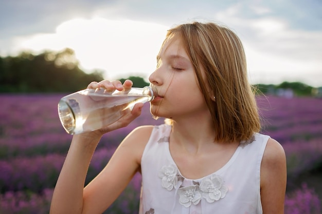 Adolescente bebe água pura de garrafa de vidro no campo de lavanda onda de calor viagens de verão
